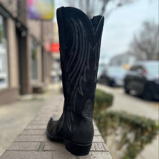 Black cowboy boot with intricate design on a stone ledge outdoors.